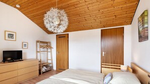 A bedroom with a wooden ceiling, a bed with white bedding, a TV on a dresser, and a wooden wardrobe. - Apartment 'Klug' with Mountain View, Private Terrace and Wi-Fi (Schonach im Schwarzwald)