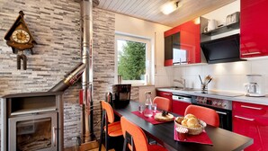 A modern kitchen with a wood-burning stove, red and white cabinets, and a dining area with orange chairs. - Apartment 'Klug' with Mountain View, Private Terrace and Wi-Fi (Schonach im Schwarzwald)
