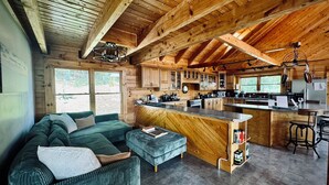 Una cabaña acogedora con interior de madera, un sofá, un comedor y una cocina con armarios de madera y una barra.