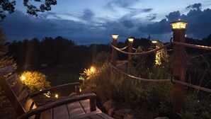 Una terraza de madera con una barandilla de cuerda, un banco y varios faroles iluminados.