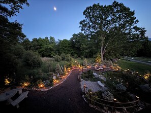 Een goed verlichte tuinpad met bankjes en kerstbomen, omringd door weelderige begroeiing en bomen.