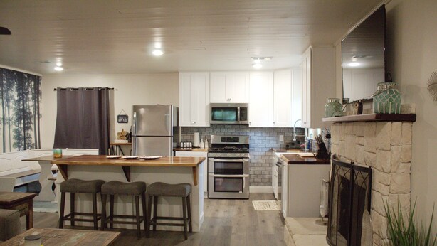 A modern kitchen with white cabinets, a built-in microwave, a stainless steel refrigerator, and a stone fireplace. - Cozy lake house w/Lake Conroe access- pet friendly! (Montgomery)