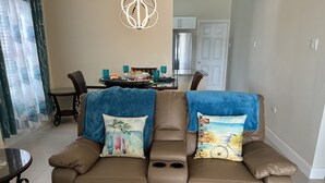 Un canapé en cuir marron agrémenté de deux coussins décoratifs, une table à manger avec des chaises, et une cuisine en arrière-plan.