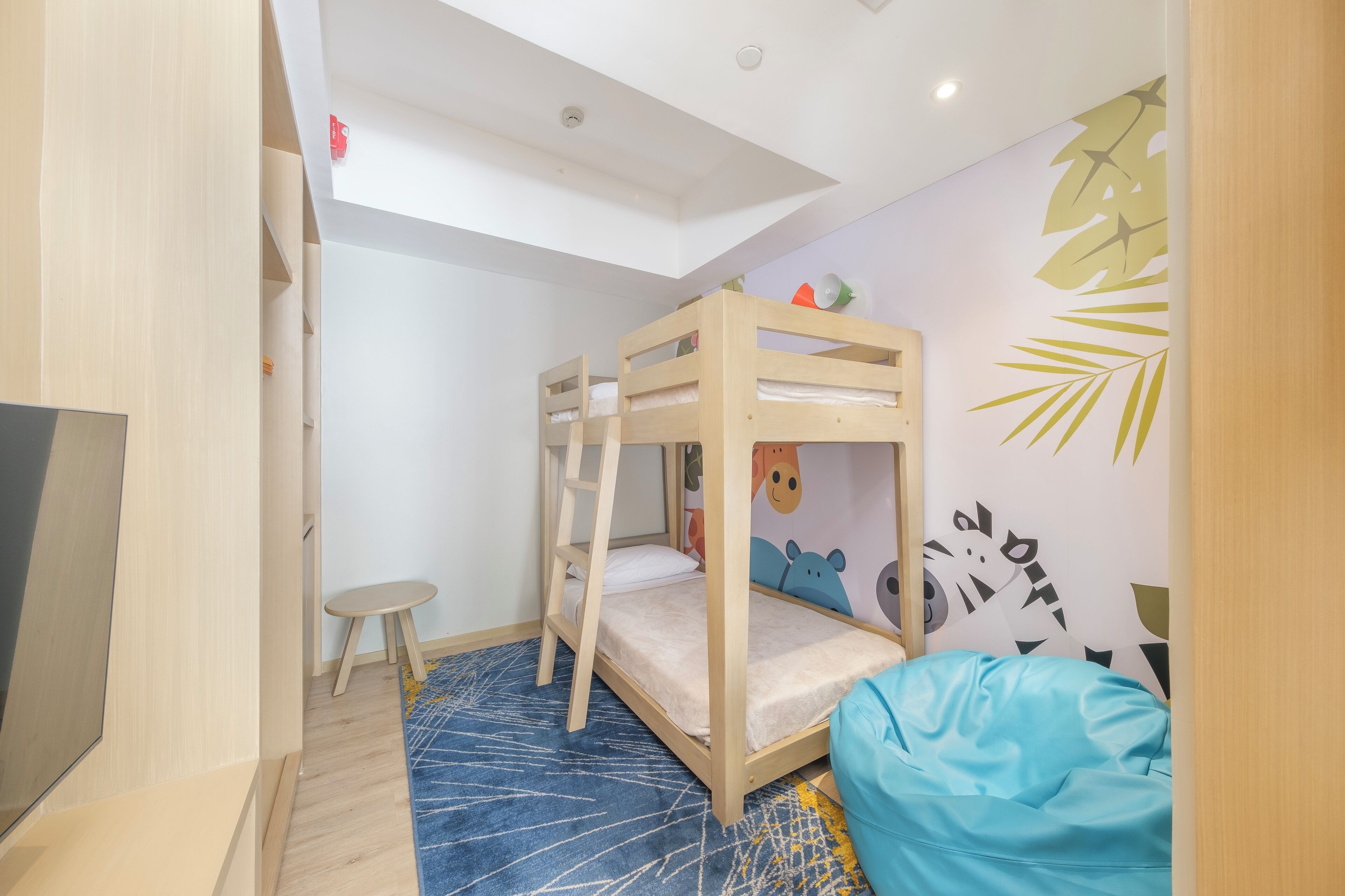 Een kamer met stapelbedden, een klein krukje, een blauwe pluchen zak en een muur met blad- en dierstickers.