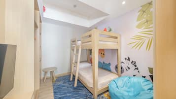 Een kamer met stapelbedden, een klein krukje, een blauwe pluchen zak en een muur met blad- en dierstickers.