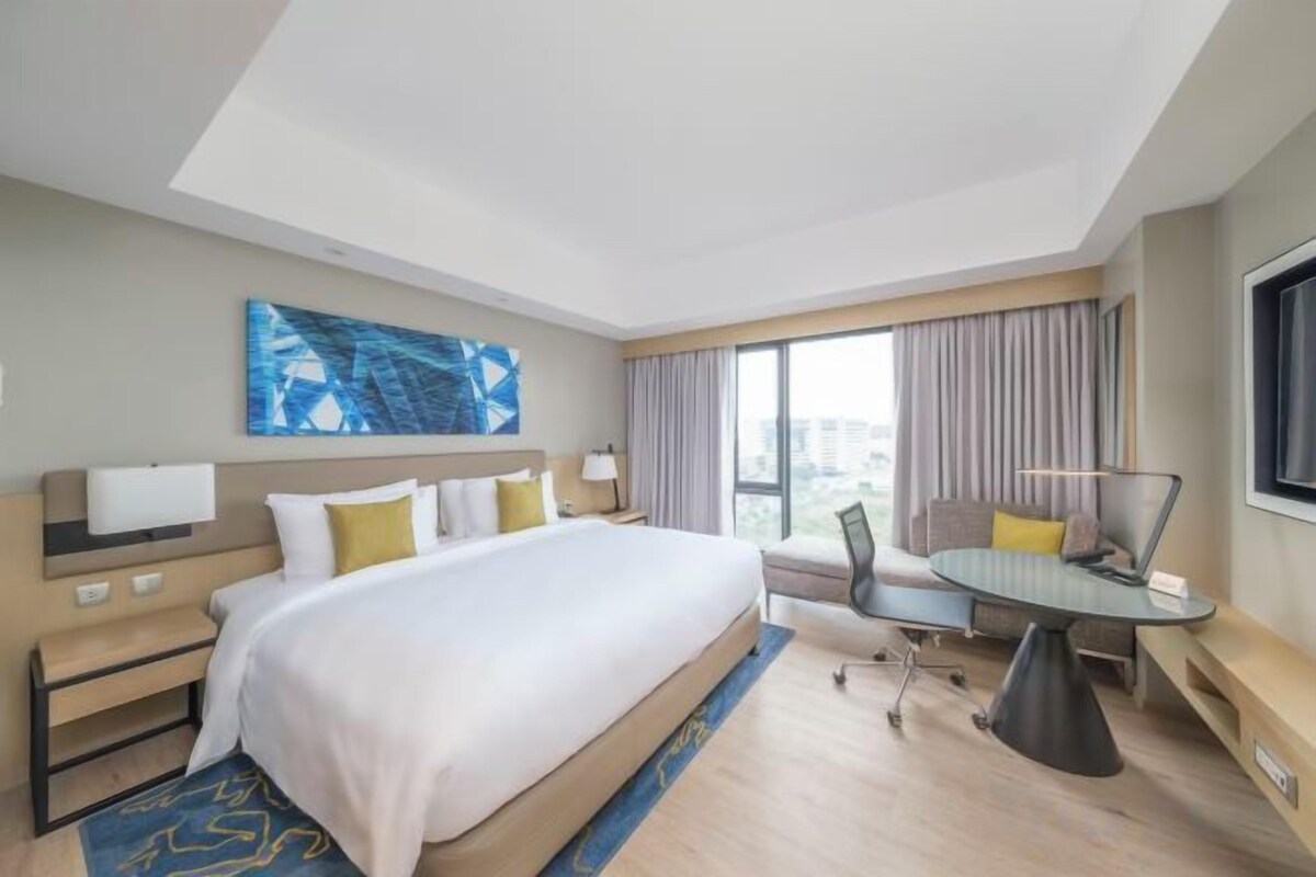 A hotel room with a large bed, a desk, and a view of the city.