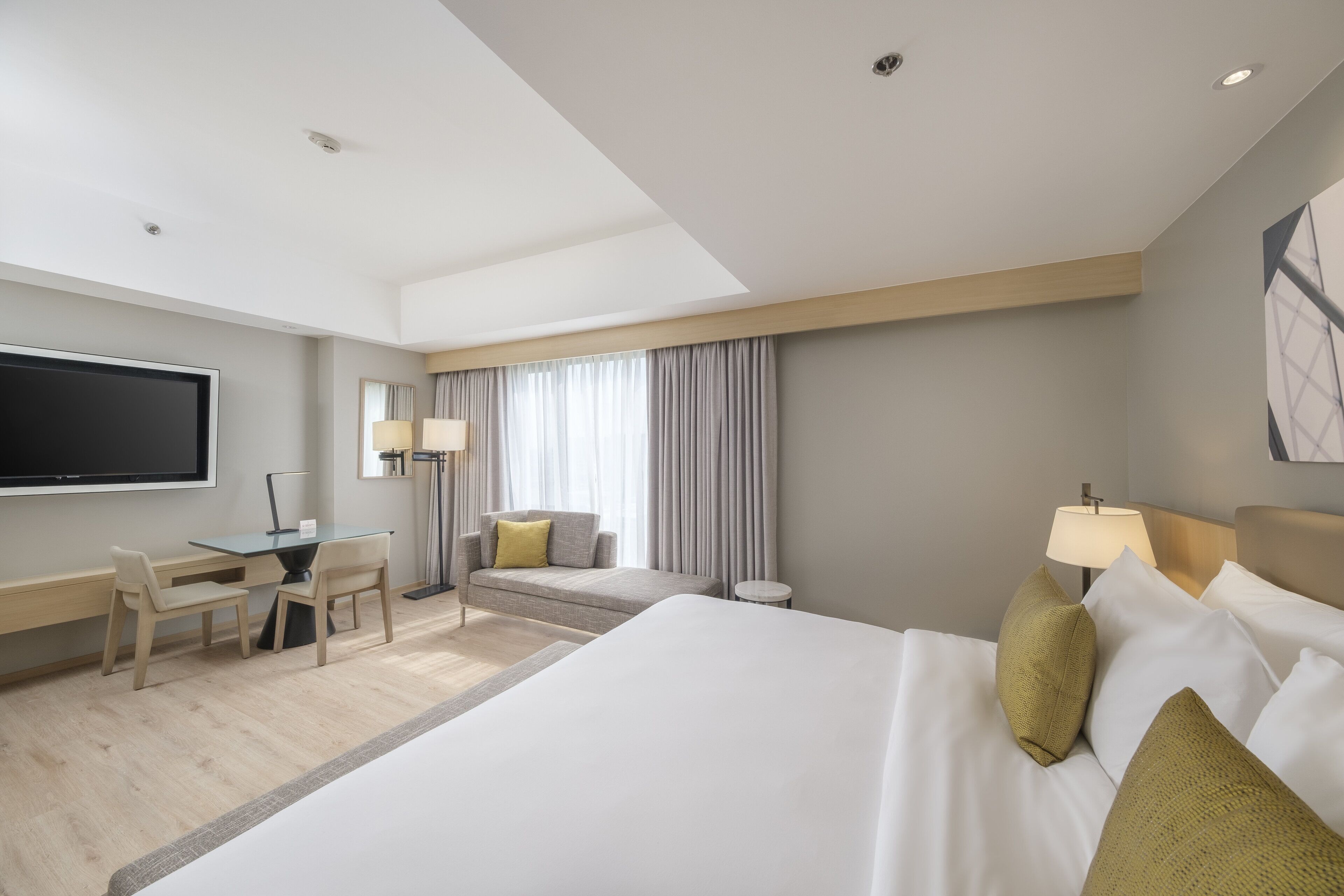 Habitación de hotel con una cama grande, un escritorio con sillas, un televisor y una ventana con cortinas.