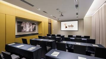 Un salón de conferencias con varias mesas y sillas, una pantalla de proyector mostrando 'soda Manila Bay', y una gran obra de arte enmarcada en la pared.