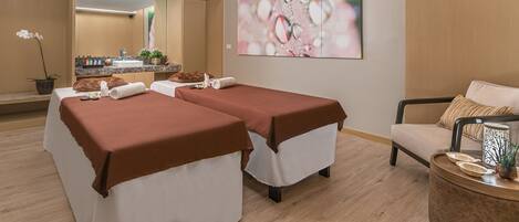A spa room with two massage tables, a sofa, a small table with decorative items, and a large mirror.