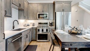 Une cuisine moderne dotée d’appareils électroménagers en acier inoxydable, de meubles en bois et d’un coin repas avec une table et des chaises en bois.