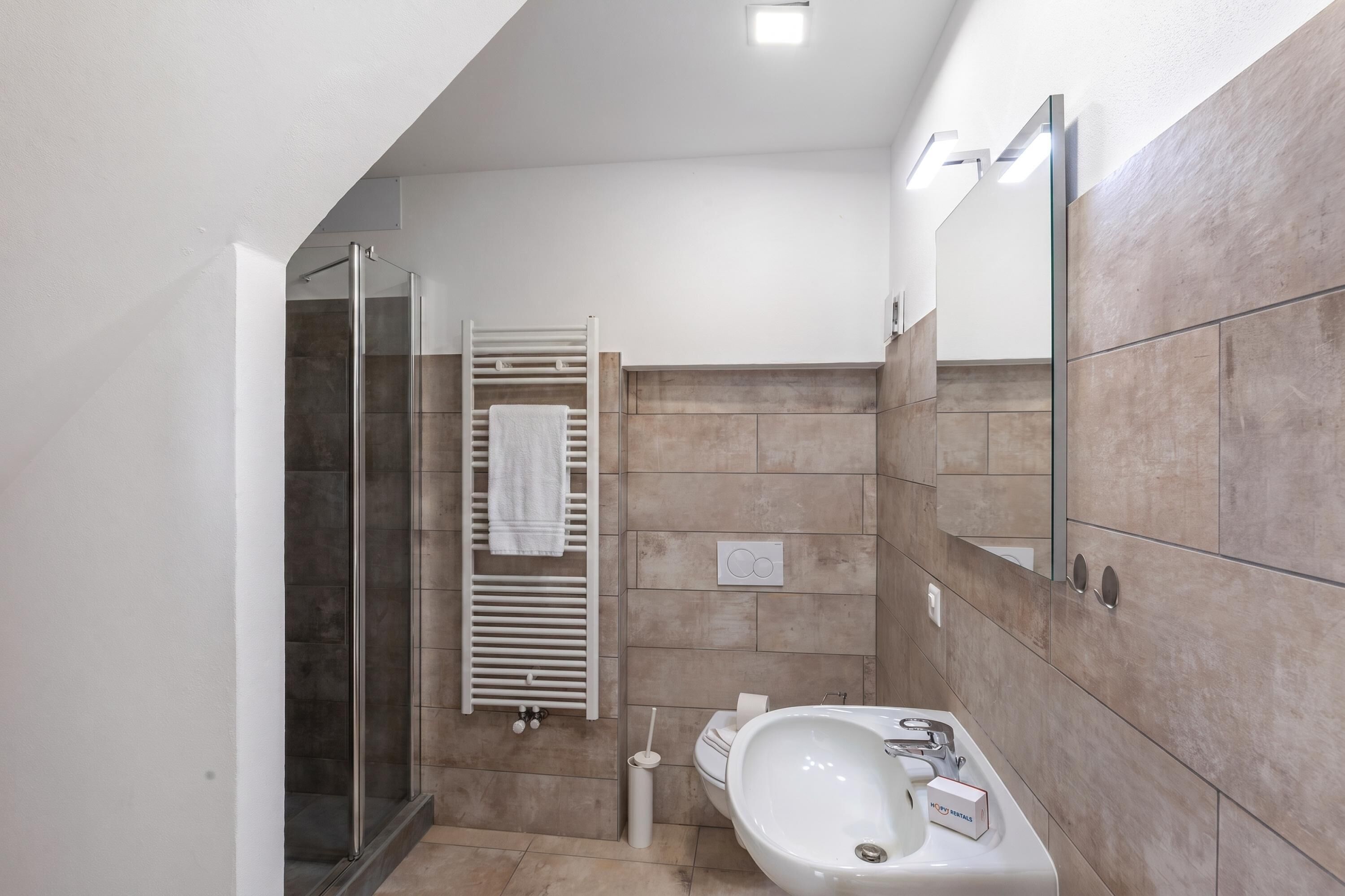 Un baño moderno con cabina de ducha de vidrio, un lavabo blanco y un perchero para toallas.