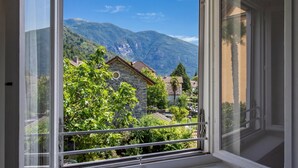 A window with a view of a mountain, a stone building, and lush greenery.
