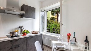 A modern kitchen with a built-in stove, a window with a view of greenery, and a dining area with a table set for two.