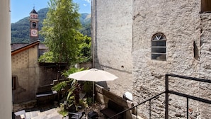 A stone building with a clock tower, a staircase, and a small patio area with a table and umbrella.