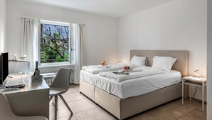 A hotel room with a bed, a desk, a chair, a TV, and a window with curtains.