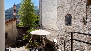 A stone building with a clock tower, a staircase, and a small patio area with a table and umbrella. - Serenata 5 - Cavigliano Studios with Terrace for 4, Cavigliano, Centovalli, Switzerland (Cavigliano, Centovalli)