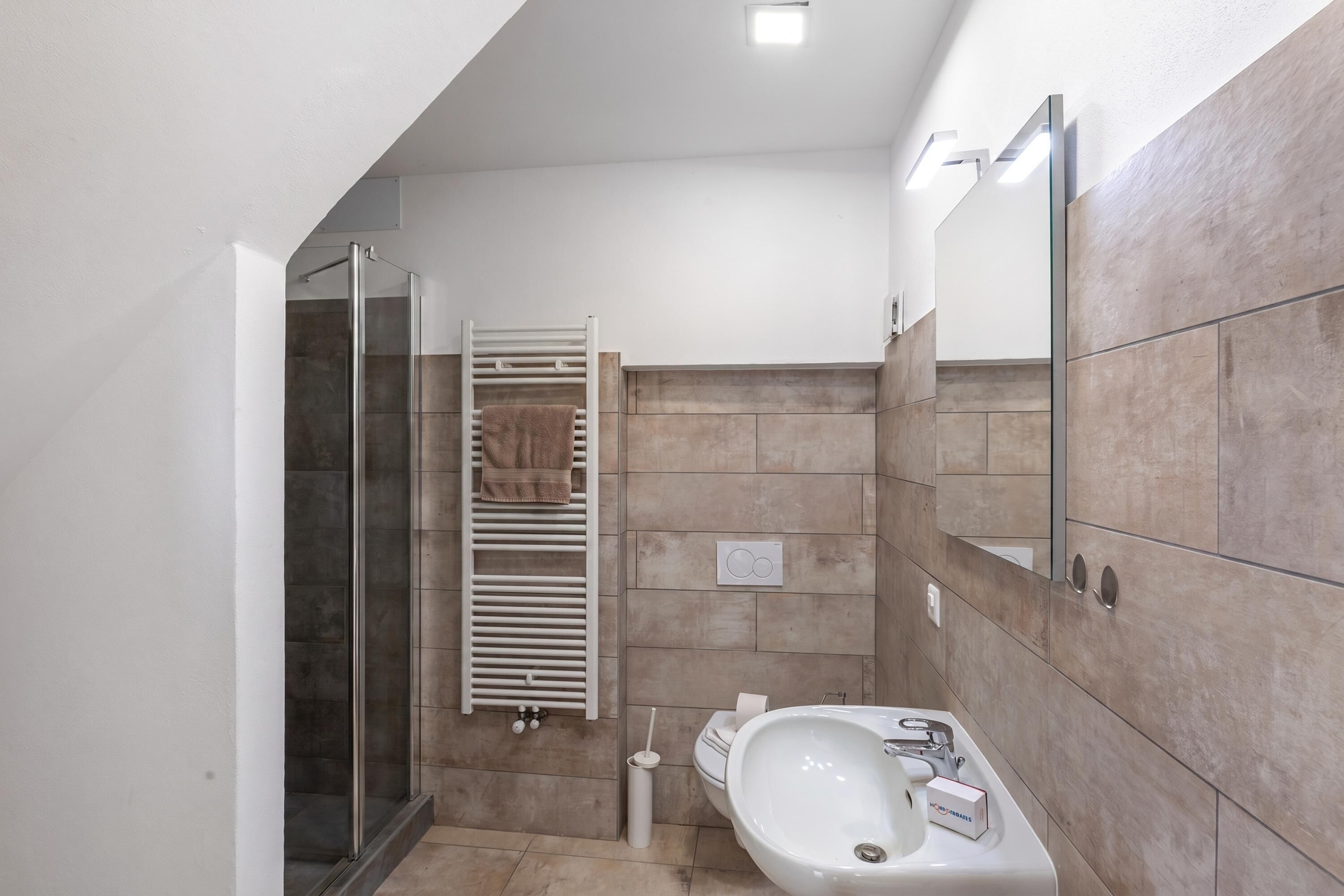 A modern bathroom with a glass shower enclosure, a built-in towel rack, a sink, and a mirror.