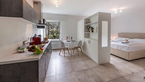 A modern kitchen with a dining area, a bed, and a view of greenery outside. - Serenata 5 - Cavigliano Studios with Terrace for 4, Cavigliano, Centovalli, Switzerland (Cavigliano, Centovalli)