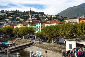 Una cittadina costiera con una chiesa imponente, un porto turistico e una folla radunata vicino a un edificio con la scritta 'ASCONA'.