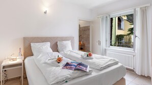 Een hotelkamer met twee bedden, een nachtkastje met lamp, een raam met gordijnen en uitzicht op buiten.