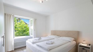 Un dormitorio con una cama grande, una mesita de noche con lámpara, una ventana con cortinas y vistas al exterior.