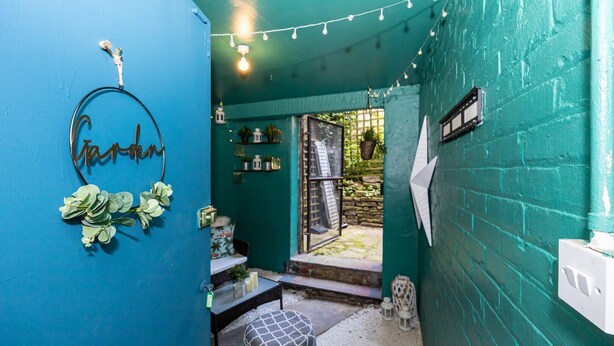 A small, enclosed outdoor space with teal walls, a metal sign reading "Garden," and a small table with a patterned cushion. - GuestReady - Charming haven in Knowledge Quarter (Liverpool)
