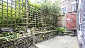 A stone wall with a wooden fence, a potted plant, and a red gate. - GuestReady - Charming haven in Knowledge Quarter (Liverpool)