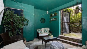 A cozy patio with a teal wall, wicker furniture, a small table, and potted plants. - GuestReady - Charming haven in Knowledge Quarter (Liverpool)