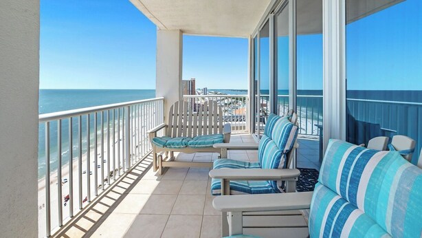 Ein Balkon mit Blick auf Strand und Meer, möbliert mit gestreiften Sofas und Stühlen.