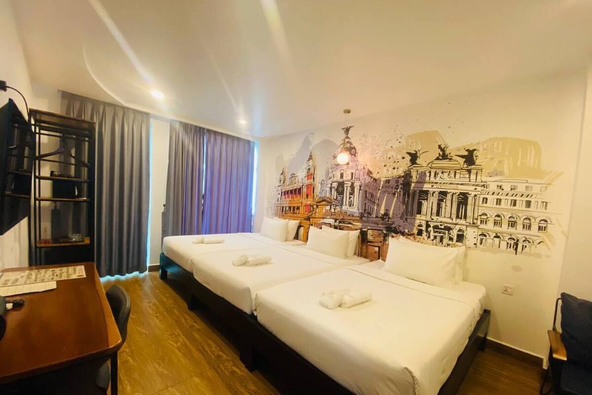 A hotel room with two beds, a wooden desk, a chair, a wardrobe, and a mural on the wall.
