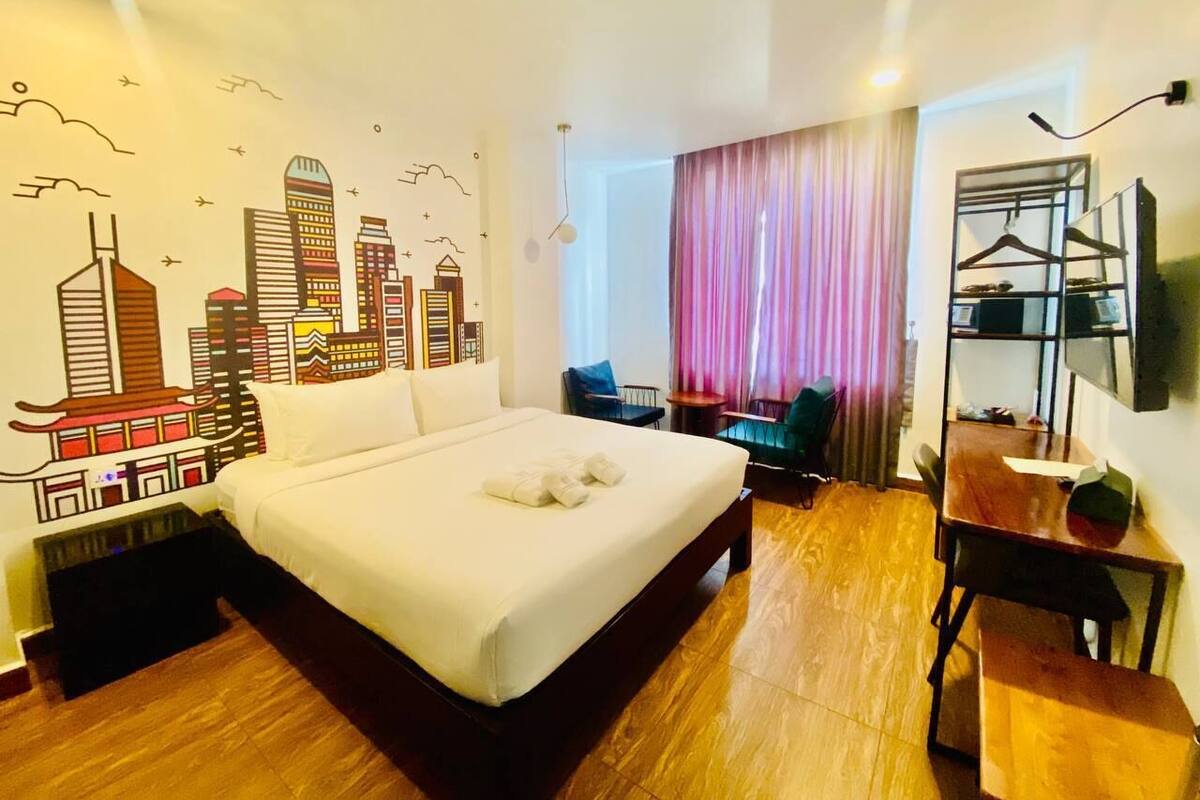 A hotel room with a large bed, a desk, a chair, and a TV mounted on the wall.