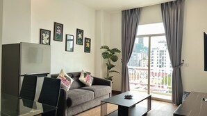 Una sala de estar moderna con un sofá gris, sillones negros, una mesa de centro de vidrio y un ventanal con cortinas grises.