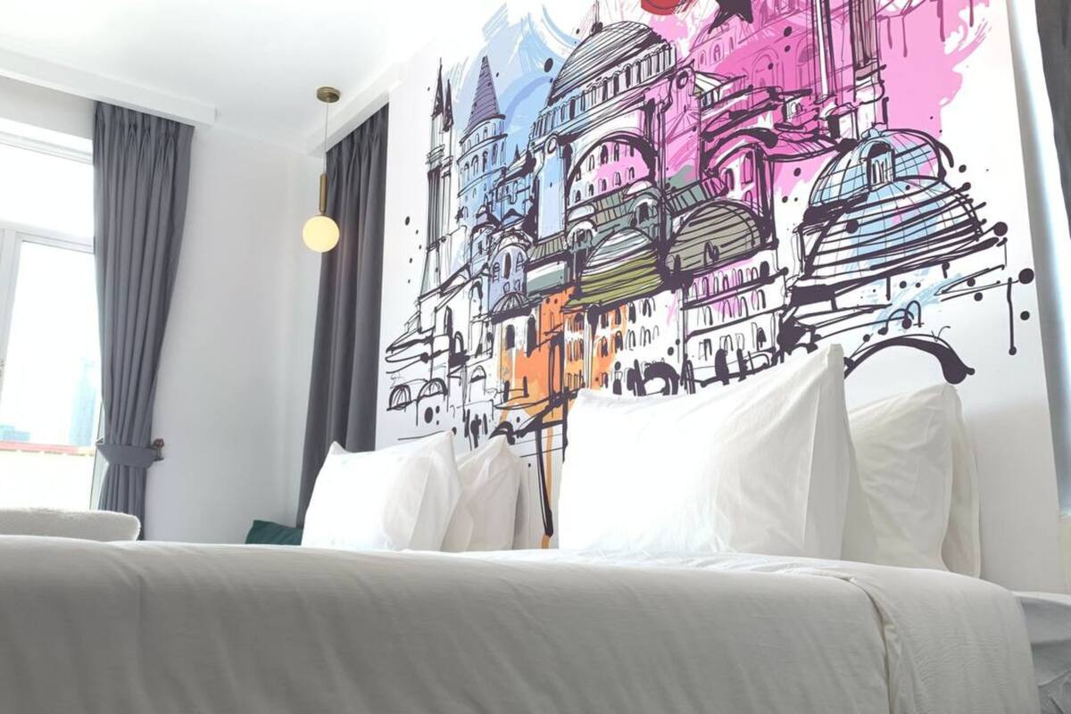 A hotel room with a large bed, a window with curtains, and a colorful mural on the wall.