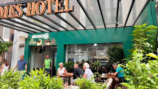 Exterior de un hotel con asientos al aire libre, un letrero de neón y un toldo verde.