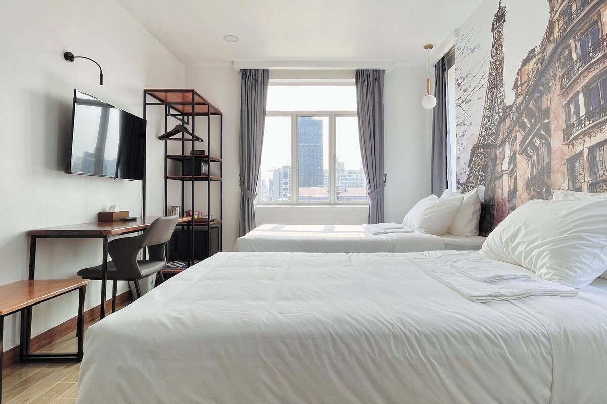 A hotel room with a bed, a desk, a chair, a TV, and a window with curtains.
