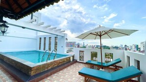 Una piscina en la azotea con jacuzzi, sillas de descanso y una sombrilla.