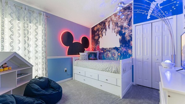 A bedroom with a Mickey Mouse themed wall, a bed with a white headboard, a desk with a computer, and a bean bag chair. - Stunning 4bed/3.5 bath pool home, great location, gated community, lake views. (Kissimmee)