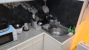 Een keuken met een magnetron, koffiezetapparaat, waterkoker en spoelbak.