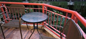 A balcony with a round table and two wicker chairs, surrounded by a red railing.