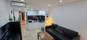 Un espacio habitable pequeño con kitchenette, un sofá, una mesa de centro y un televisor.