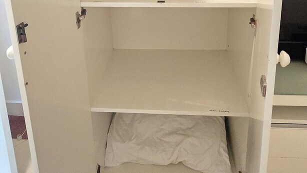 Een kamer met een witte kast met drie planken, een witte handdoek op de onderste plank, en een betegelde vloer.