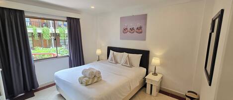 A hotel room with a bed, two bedside tables, a window with curtains, and a wall-mounted artwork.