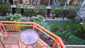 Een balkon met een tafel en stoelen, omgeven door groen en een uitzicht op een binnenplaats met meerdere niveaus.