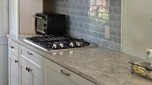 Una cocina con armarios blancos, estufa a gas, tostadora y salpicadero de azulejos.