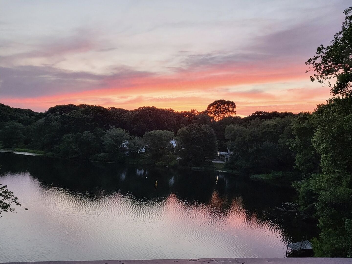 A serene lakeside view with trees and a clear sky at sunset.