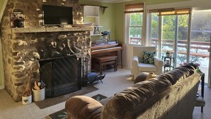 Un salón acogedor con chimenea de piedra, un piano, un televisor y un ventanal con vistas.