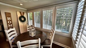Une salle à manger avec une table ronde, des chaises blanches, une enseigne en bois sur laquelle on peut lire le mot « MAISON », et une guirlande accrochée au mur.