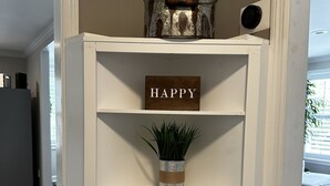 Une étagère blanche sur laquelle on voit un panneau indiquant « JOYEUX », des livres et une plante.