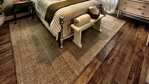 Une chambre à coucher comprenant un lit, des tables de chevet, un banc, un ventilateur de plafond et une commode.
