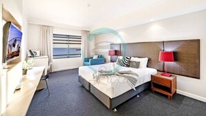 A hotel room with a bed, a desk, a chair, a TV, a window, and a nightstand. - ZEN88 ESPLANADE - Hotel Suite Ocean View (Darwin)